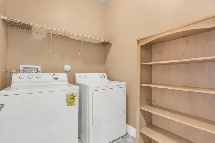 Utility room featuring white top-load laundry appliances, wall-mounted wire shelving, and built-in light wood cabinetry