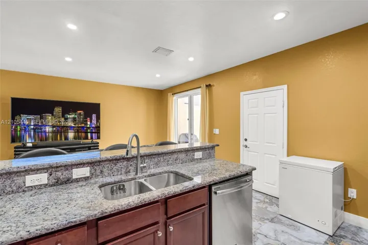 Kitchen featuring a peninsula with stone-look countertop, undermount stainless steel double-basin sink with gooseneck faucet, dark-finish cabinetry, stainless steel dishwasher, and tile flooring