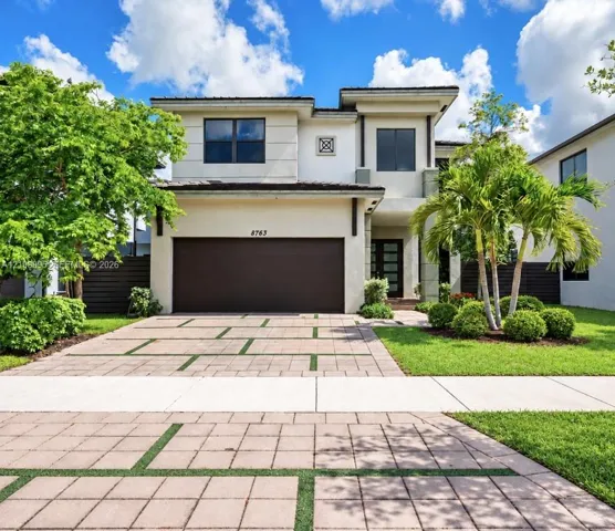 Contemporary two-story exterior featuring a stucco façade, clean geometric architectural lines, a multi-car garage, and a paver driveway with integrated turf strips
