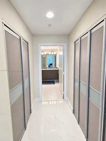 Hallway featuring large-format tile flooring and dual wall-to-wall closets with sliding panel doors, recessed ceiling lighting, and brushed metal trim