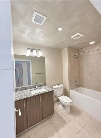 Bathroom featuring a stone-look countertop, wood-finish cabinetry, a large wall-mounted mirror, recessed lighting, and a tiled shower-tub combination