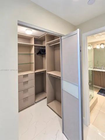 Walk-in closet featuring custom built-in cabinetry, integrated shelving, glass display surfaces, and a sliding door with frosted panel inserts