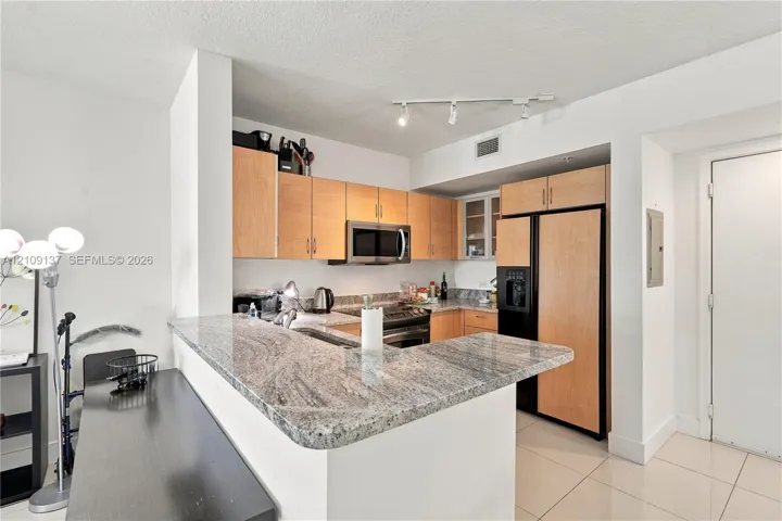 Kitchen featuring light-finish cabinetry, stone countertops, a breakfast bar, stainless steel microwave, and tile flooring