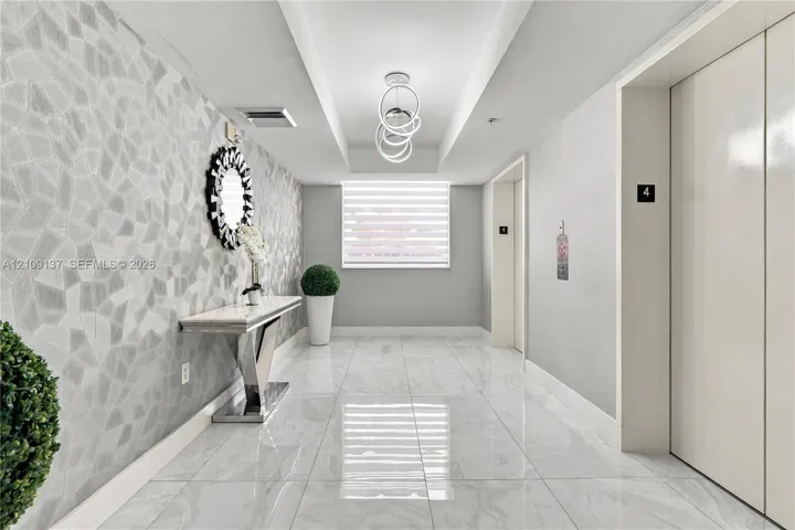 Entryway featuring large-format polished tile flooring, geometric textured wall covering, recessed ceiling detail, and contemporary ring chandelier