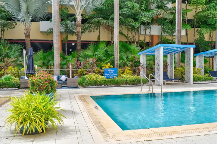 Swimming pool with masonry coping, paver patio, and integrated shade structures surrounded by lush tropical landscaping