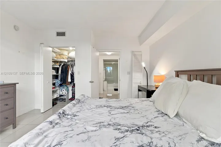 Neutral-toned room with tile flooring, featuring a walk-in closet with built-in shelving, louvered closet doors, and smooth ceiling finish