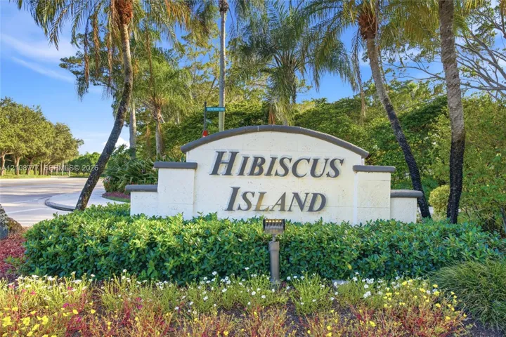 Custom stone community monument sign featuring raised lettering, integrated landscape lighting, and professional xeriscaping with mature palm trees and flowering shrubs