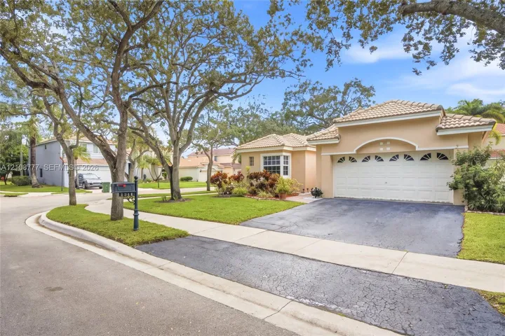 Single-story residence featuring a stucco exterior, a multi-car garage with arched decorative glass detailing, tile roofing, and mature trees