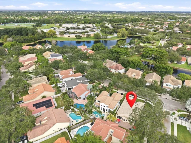 Aerial perspective showcasing a residential property with a tiled roof, paver hardscaping, and mature landscaping, situated within a master-planned community featuring multiple ponds and dense tree canopy