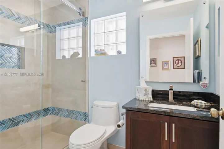 Full bathroom featuring a walk-in shower with glass sliding door and decorative herringbone-pattern tile inlay, a dark wood-finish vanity with a dark stone countertop, an integrated sink, and glass block windows