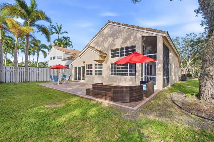 Stucco exterior featuring a screened-in lanai, paver patio, and mature palm trees