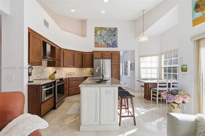 Kitchen featuring vaulted ceilings, a central island with a stone countertop, stone-finish flooring, stainless steel appliances, and wood cabinetry