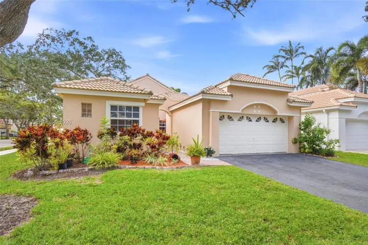 Single-story residence featuring a tile roof, stucco exterior, arched garage entry with decorative glass detailing, and manicured landscaping