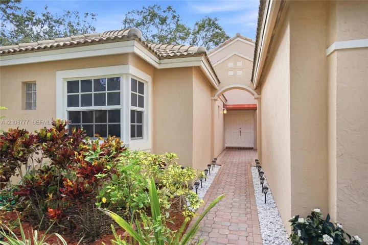 Stucco exterior with a tile roof, featuring a paver walkway, arched entryway, bay window, and built-in exterior lighting