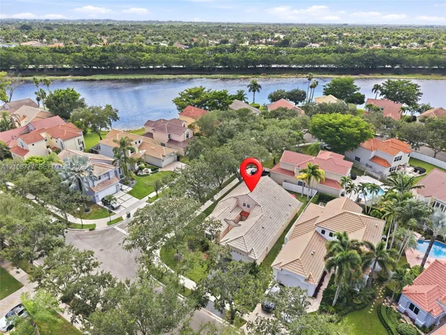 Aerial perspective of residential property featuring a multi-pitched tile roof, attached garage, paved driveway, and mature landscaping
