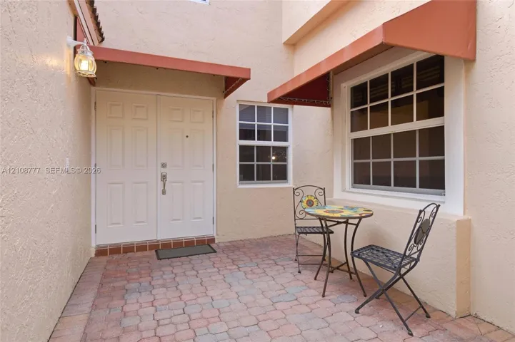 Courtyard entrance featuring a paved stone patio, double-door entry, multi-pane windows, and fixed exterior metal awnings