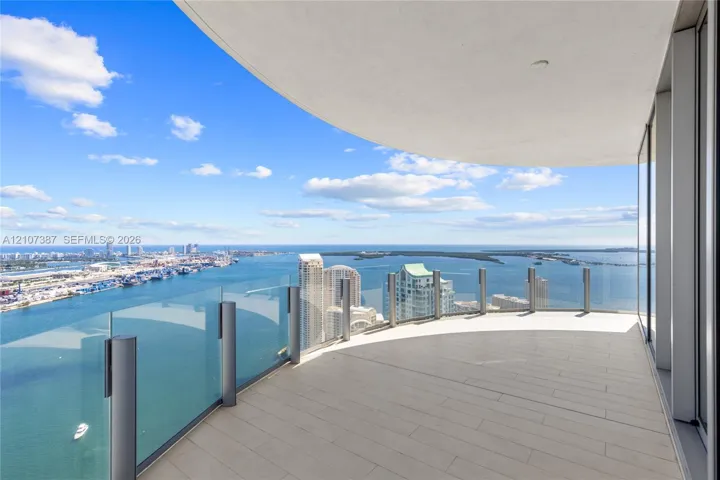 Curved balcony featuring tile flooring, glass panel railings, and panoramic coastal and urban scenery