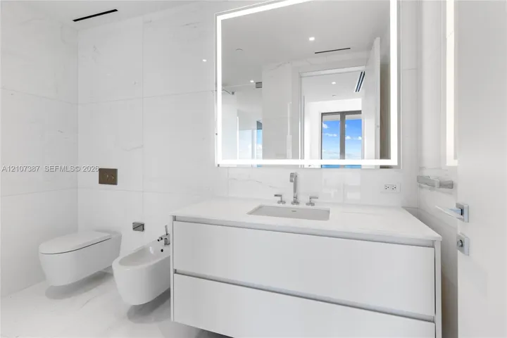 Modern floating vanity with a seamless countertop, wall-mounted commode and bidet, large-format tile wall cladding, and an integrated LED backlit mirror