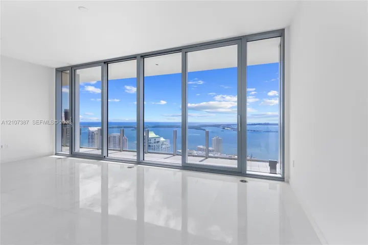 Floor-to-ceiling glass panel windows, sliding glass door, polished tile flooring, and private balcony with metal and glass railing