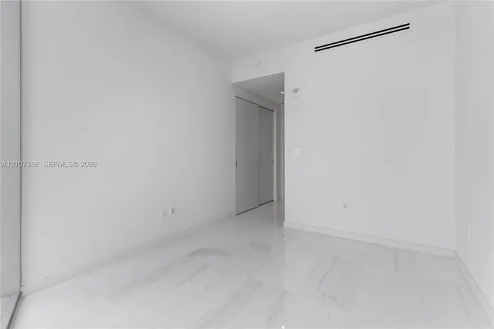 Minimalist interior space featuring polished light-toned stone flooring and dual-panel sliding closet doors