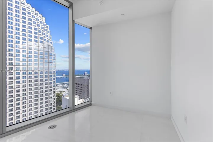 Floor-to-ceiling windows featuring expansive urban and water scenery, complemented by crisp white walls and light-toned tile flooring