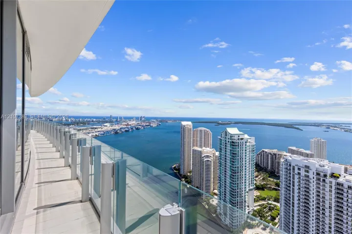 Curved wrap-around balcony featuring glass panel railing, tile flooring, and expansive water and urban skyline scenery