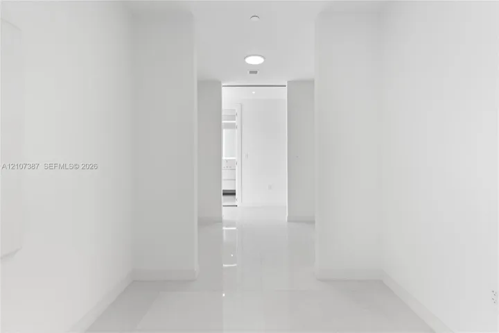 Interior corridor featuring polished stone-finish tile flooring, clean white walls, and recessed ceiling lighting