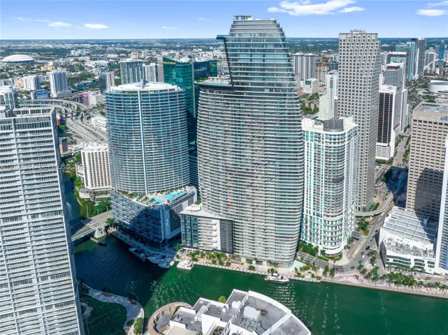 High-rise residential tower featuring a glass-curtain facade, prominent tiered architectural design, and water frontage along a canal