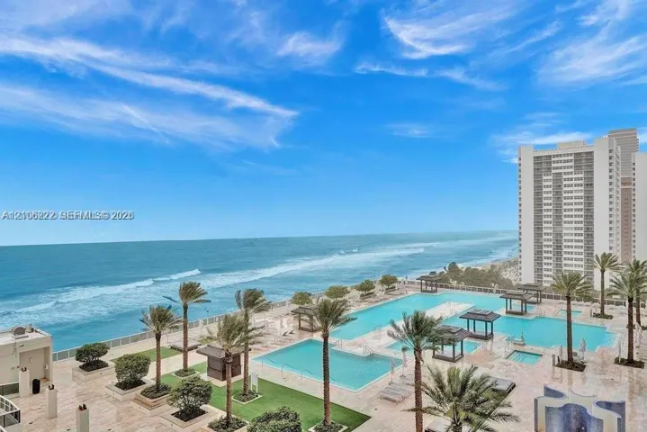 Oceanfront terrace featuring multiple swimming pools, stone-paved decking, built-in pergolas, and established palm trees