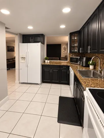 Kitchen featuring dark wood cabinetry, stone countertops, stainless steel sink with a high-arch faucet, light-toned floor tile, and recessed lighting