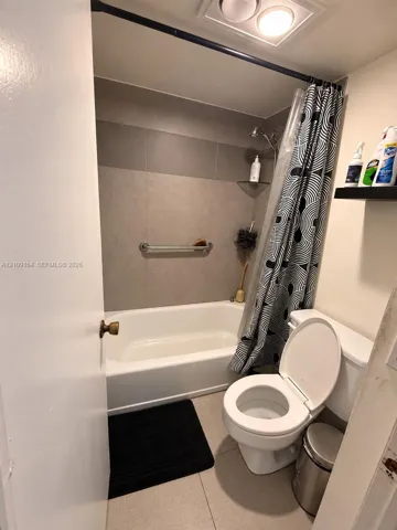 Full bathroom featuring a white bathtub with a tiled surround, a metal grab bar, a wall-mounted glass corner shelf, and a ceiling-mounted light fixture