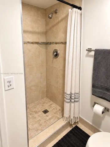 Walk-in shower featuring floor-to-ceiling tile, an integrated accent border, textured stone-style shower floor, and brushed-finish fixtures
