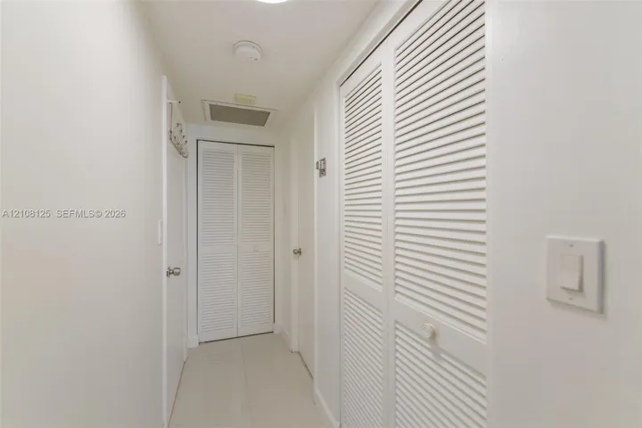 Hallway featuring high-gloss tile flooring, white-painted walls, and dual sets of white louvered-panel closet doors