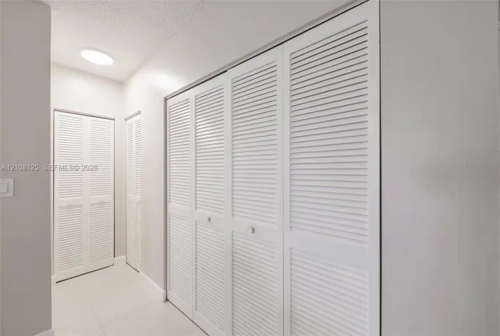White louvered closet doors, neutral wall finish, and tile flooring