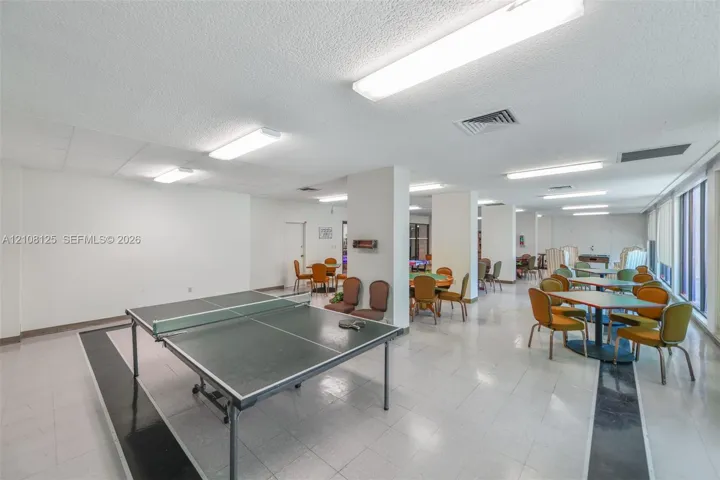 Open-concept interior space featuring ceramic tile flooring with decorative dark accents, structural support columns, and multiple flush-mount linear lighting fixtures