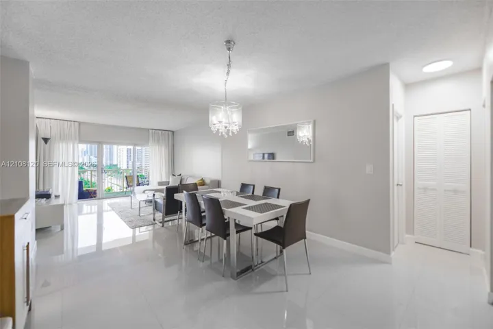 Open-concept living space featuring high-gloss tile flooring, an ornate crystal chandelier, a large wall-mounted mirror, and white louvered-panel closet doors