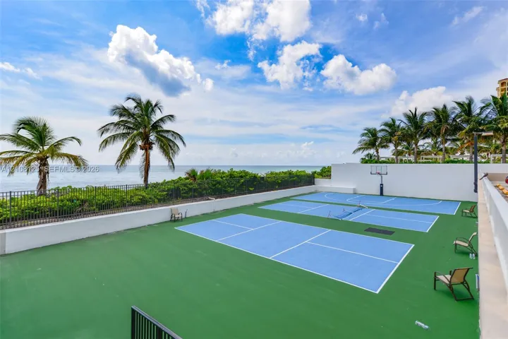 Multi-sport court featuring pickleball and basketball configurations, surrounded by perimeter wall fencing, set against an ocean backdrop with mature palm trees