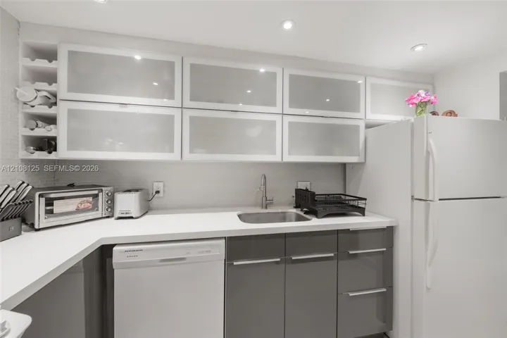 Kitchen featuring high-gloss charcoal base cabinetry, upper cabinets with frosted glass inserts, solid-surface countertops, recessed ceiling lighting, and integrated wine storage