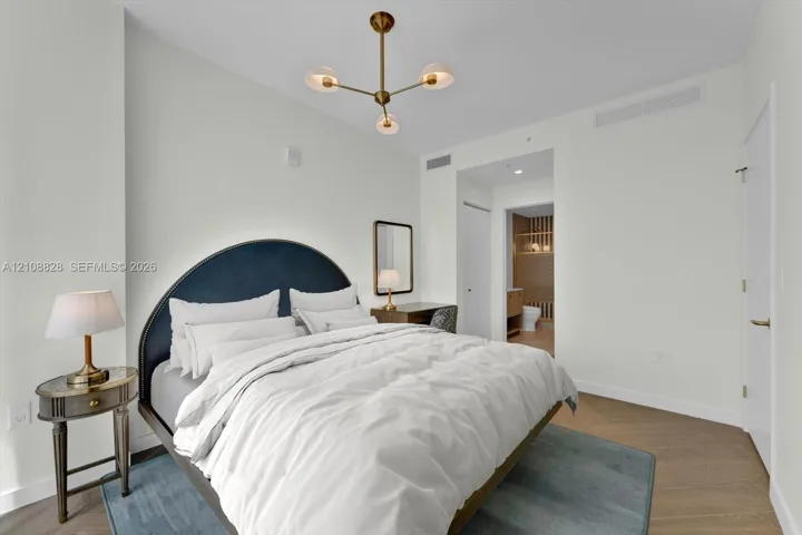 Modern bedroom featuring wood-finish flooring, a multi-arm brass finish chandelier, and neutral wall color