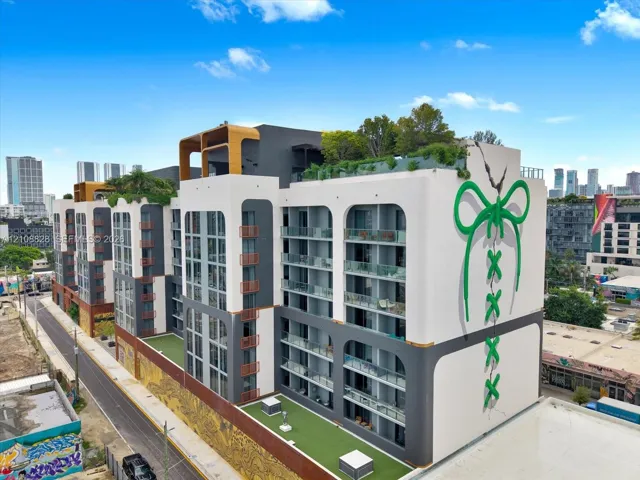 Multi-story modern exterior featuring arched structural elements, glass-panel balconies, rooftop terrace space, synthetic turf lower-level patios, and large-scale exterior mural art