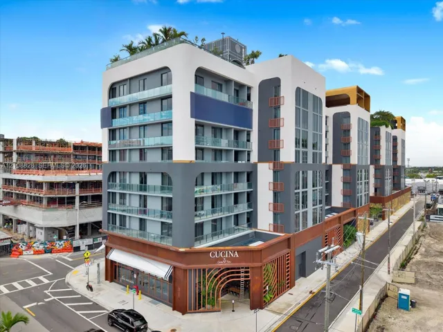Modern multi-story structure featuring a stucco exterior with tiered balconies, glass railings, metal-slat design elements, and a ground-level commercial storefront