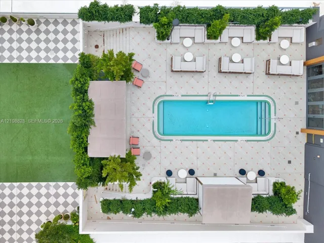 Outdoor terrace featuring a rectangular swimming pool, manicured greenery, artificial turf section, and decorative tile paving