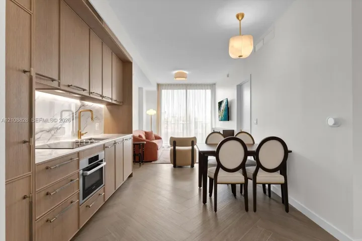 Kitchen featuring light wood-finish cabinetry, integrated appliances, stone-surface backsplash, and gold-toned hardware, complemented by herringbone-pattern flooring