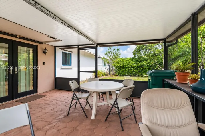 Screened-in patio featuring hexagonal paver flooring, a solid panel roof, and black-framed exterior French doors with glass panes