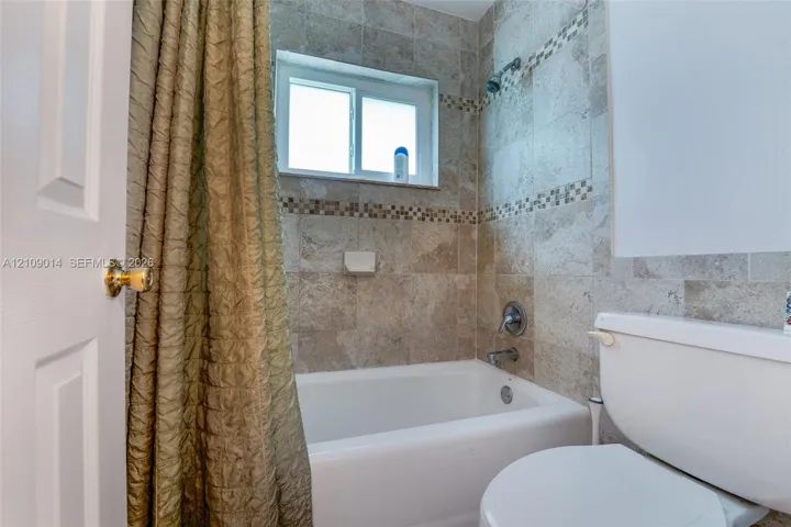 Full-height tile shower surround with decorative mosaic inlay, integrated bathtub, and sliding glass window