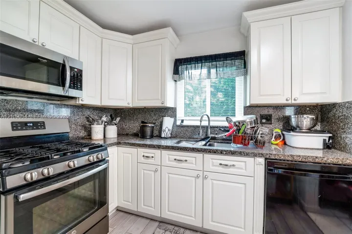 Kitchen featuring white shaker-style cabinetry, stone-finish countertops, full-height stone backsplash, stainless steel gas range, and over-the-range microwave