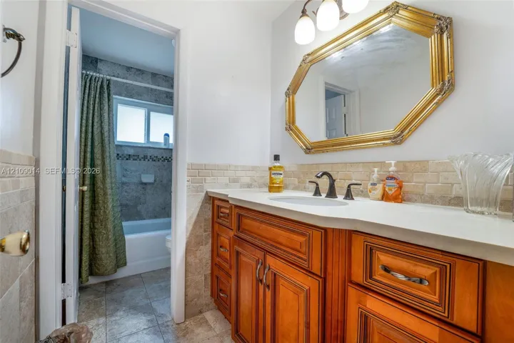 Bathroom vanity featuring wood cabinetry, integrated basin, stone-tiled backsplash, and multi-light fixture with an octagonal framed mirror