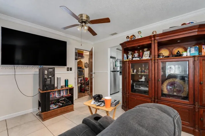 Living area featuring ceramic tile flooring, crown molding, chair rail trim, and a ceiling fan with integrated lighting