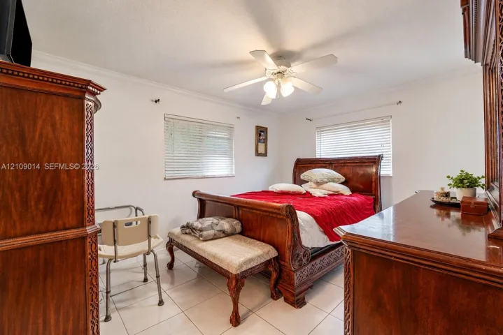 Room featuring neutral wall finishes, tile flooring, crown molding, a central ceiling fan with integrated lighting, and two windows with horizontal blinds