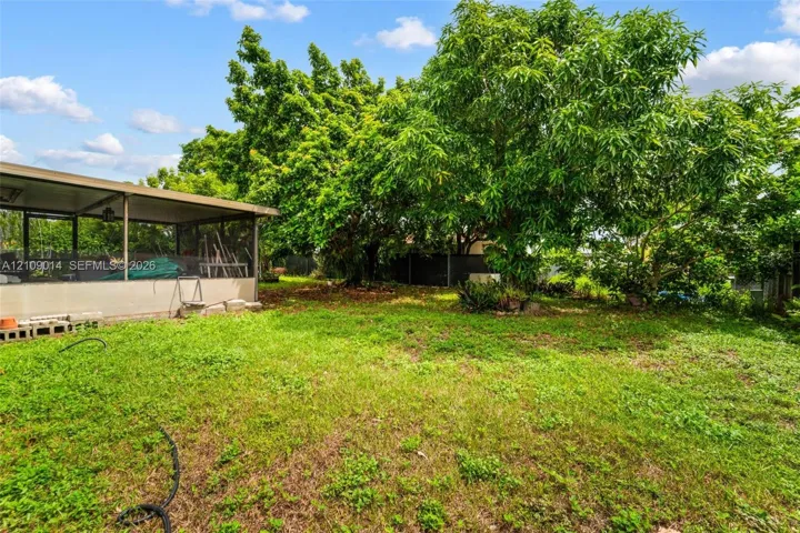Screened-in outdoor enclosure featuring a metal roof structure, expansive lawn area, and mature shade trees